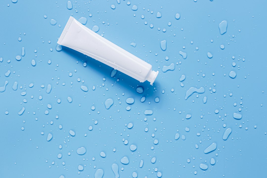 An unlabelled white skincare tube on a blue background with water droplets.