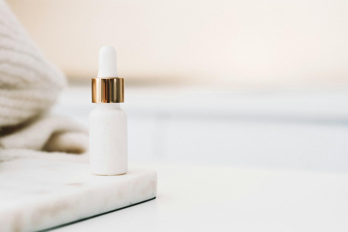 White dropper bottle beside a folded towel on a pale surface